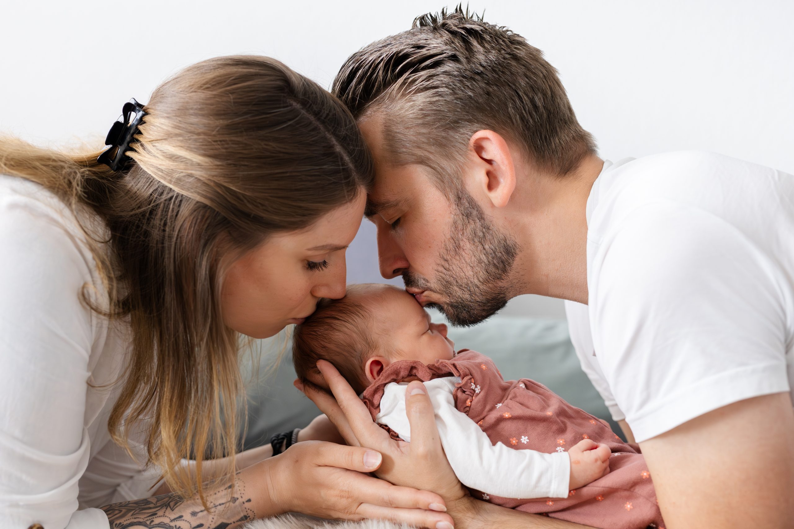 Papa und Mama küssen das Baby - zarte und liebevolle Erinnerung an die erste Zeit mit Baby im eigenen Zuhause